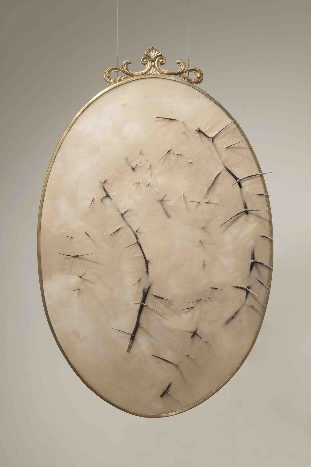 An oval artwork with gold frame, beige texture, and dark thorns protruding across the surface.
