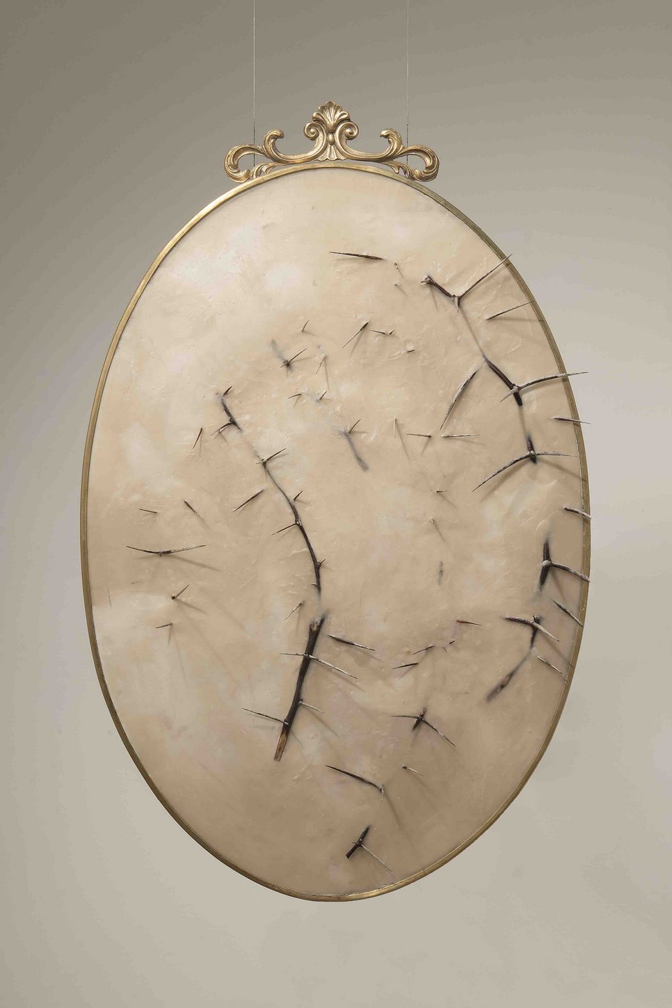 An oval artwork with gold frame, beige texture, and dark thorns protruding across the surface.