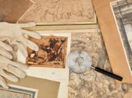 Diverse historische Zeichnungen, eine Lupe und weiße Handschuhe liegen auf einem Tisch.