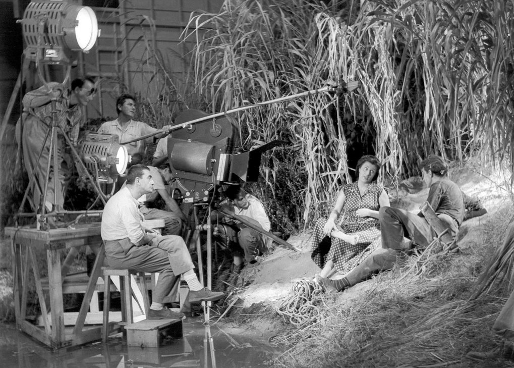 Film crew working on a set with cameramen and lighting, while two people sit in the foreground.