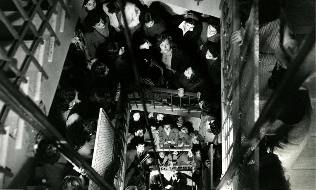 Large group of people on a staircase, all looking up, in a busy stairwell.