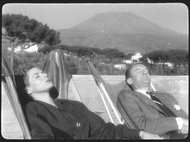Two people relax in deck chairs with a mountain in the background.