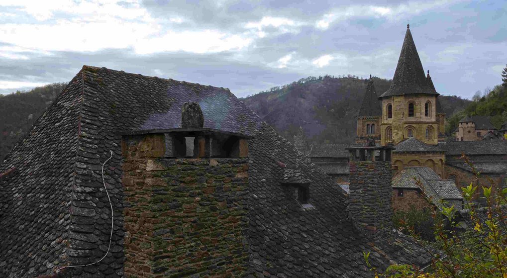 Historische Steindächer und Schornsteine, Turm ragt hinter Hügeln hervor.