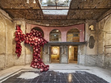 Rote Skulptur aus großen Kugeln in einem verfallenen Raum mit Marmorwänden.
